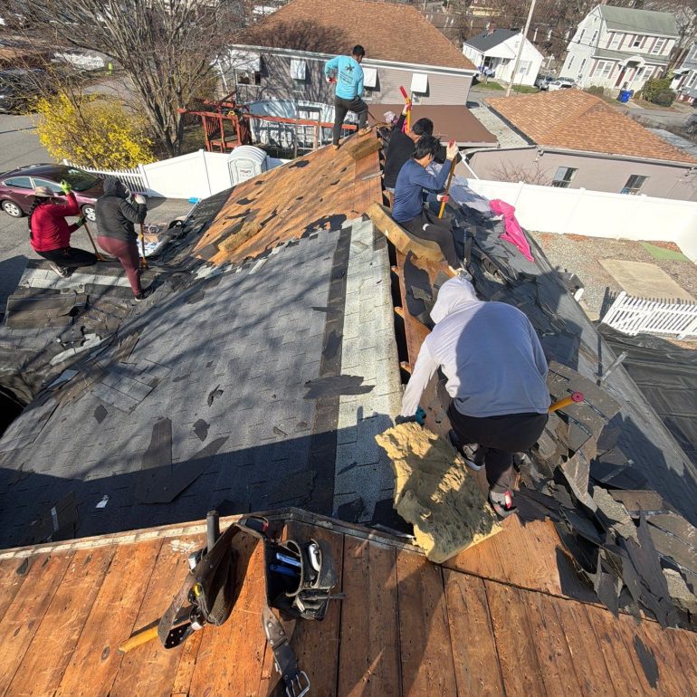 flat roof vs sloped roof pros and cons roof replacement Roofing contractors removing old shingles during a sloped residential roof replacement for flat roof vs sloped roof comparison guide.
