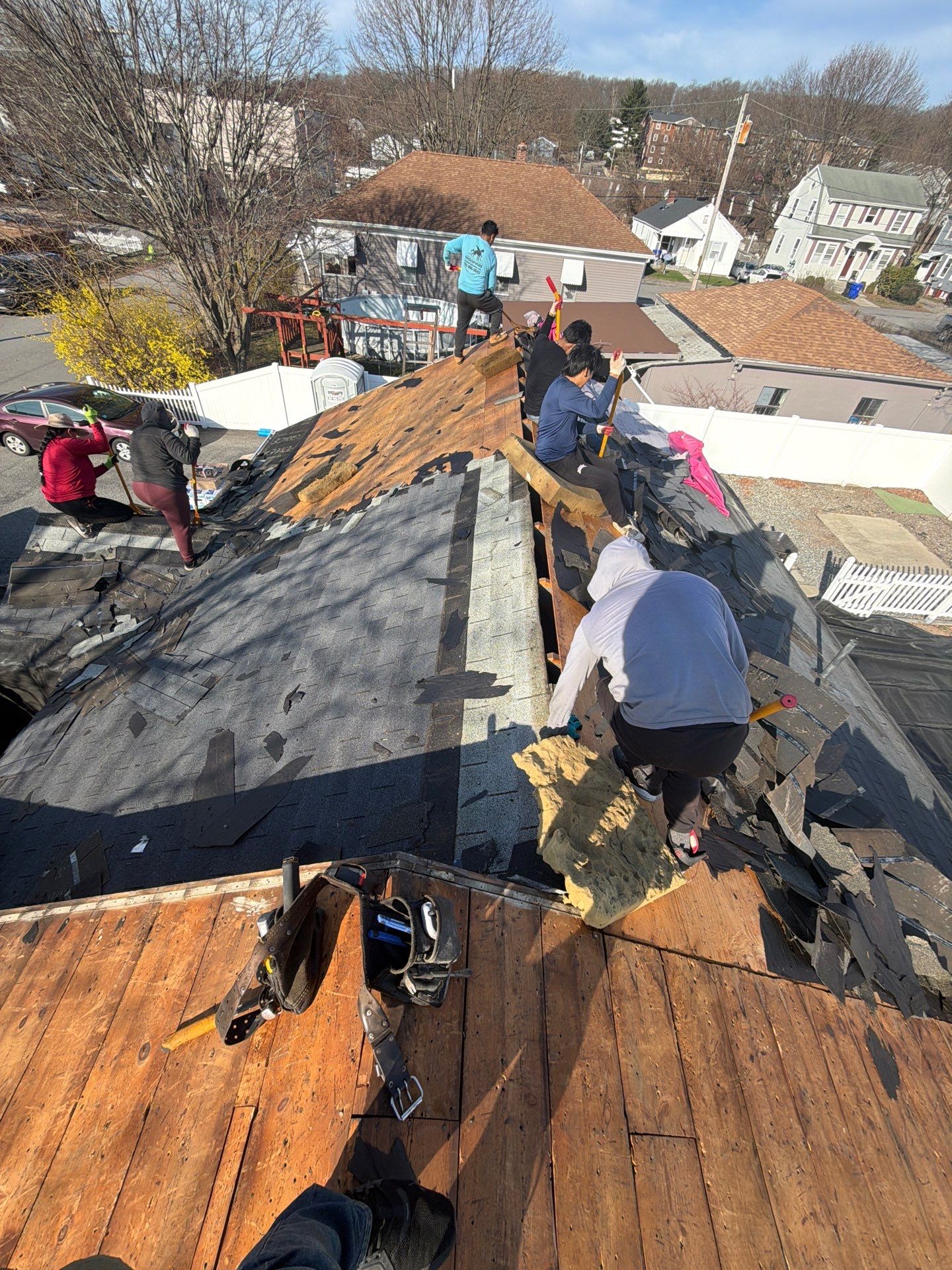 flat roof vs sloped roof pros and cons roof replacement Roofing contractors removing old shingles during a sloped residential roof replacement for flat roof vs sloped roof comparison guide.