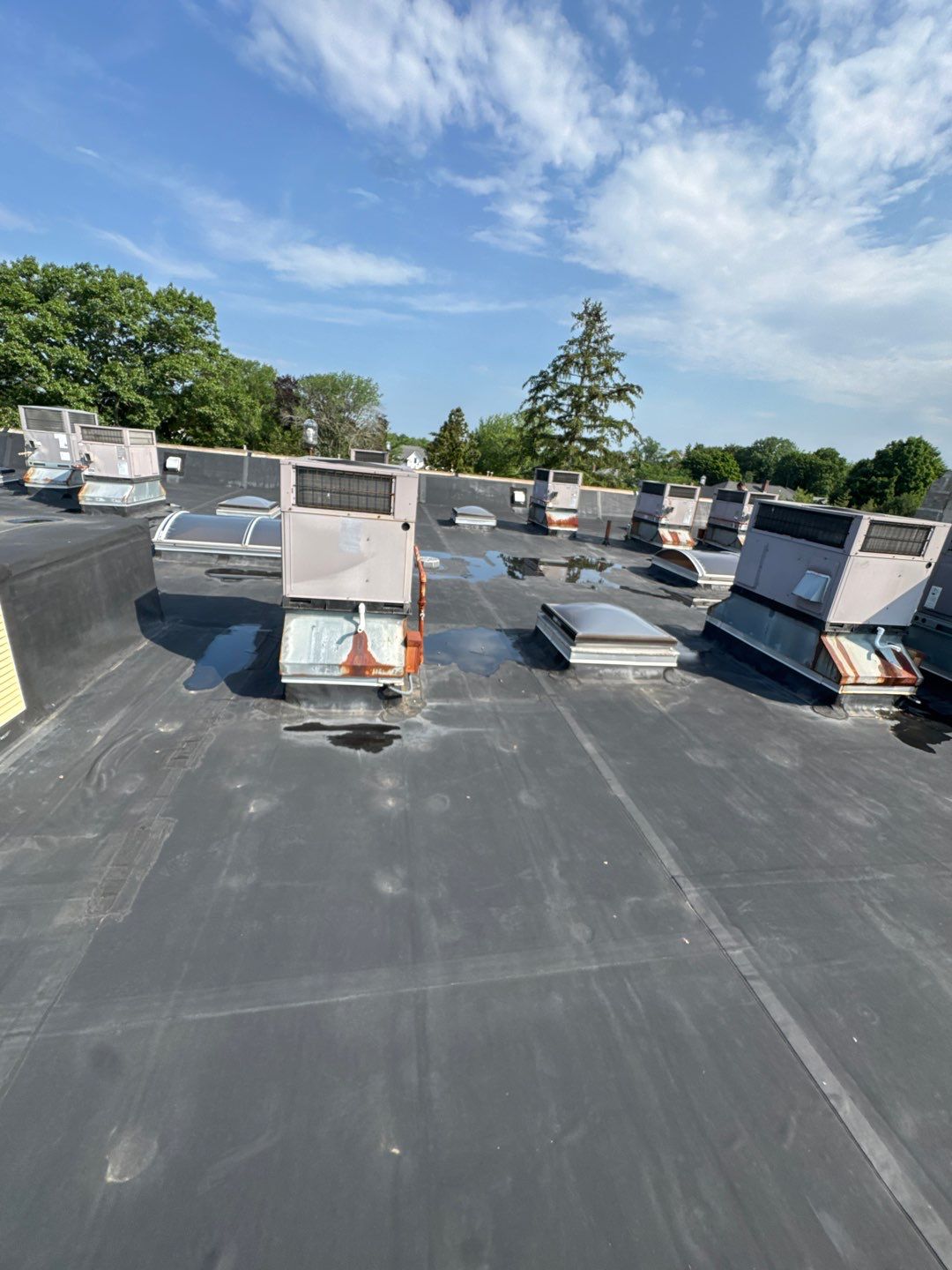commercial flat roof leak detection Commercial flat roof leak detection inspection showing ponding water around rooftop HVAC units on a membrane roofing system.