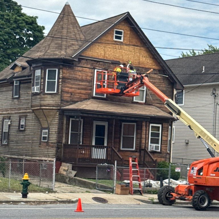 residential wood siding replacement Contractors performing residential wood siding replacement on a two-story home using a boom lift during exterior renovation.